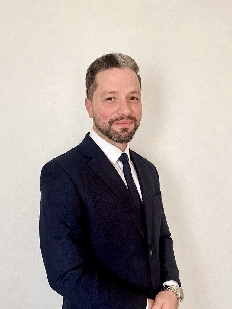 Ahmad Yousef in a navy suit, smiling, against a pale wall